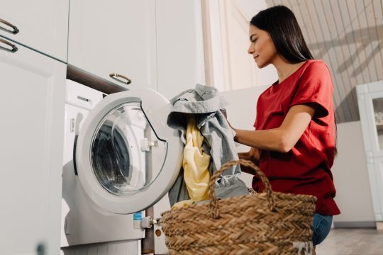 Young,Hispanic,Brunette,Woman,Putting,Clothes,At,Washing,Machine,While